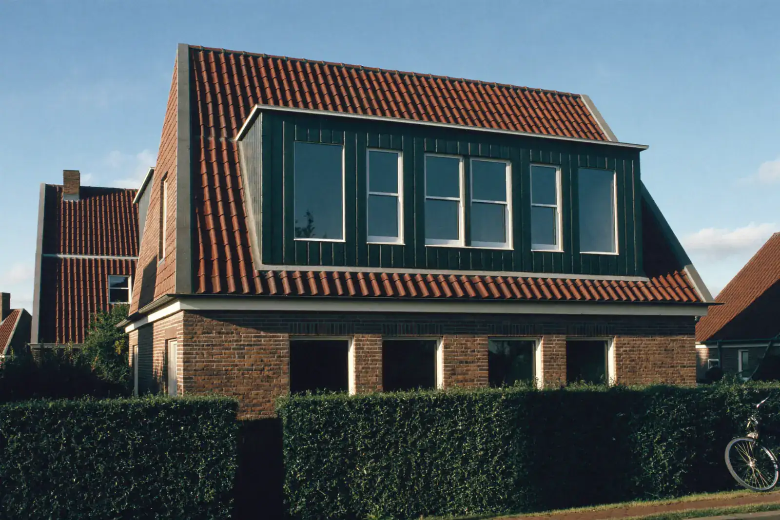 Brede donkergroene dakkapel met meerdere ramen die bijna tot de nok van een pannendak loopt