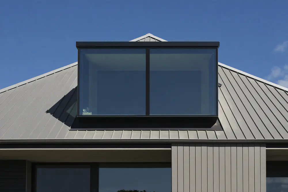 Dakkapel met slanke zwarte aluminium kozijnen en veel glas op een grijs dak met zink